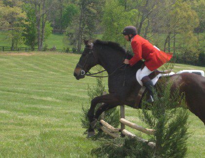 Rider in red coat jumping horse in field