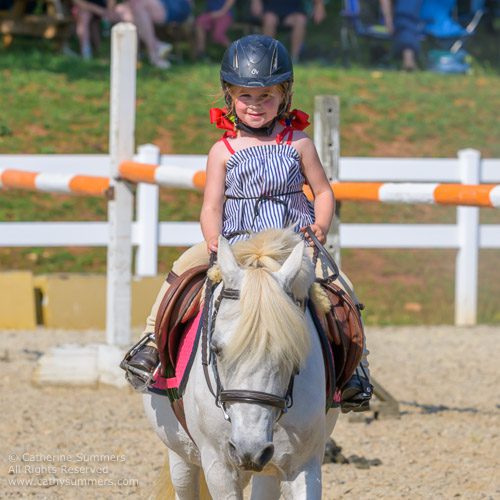 cute kid on a pony, braids and ribbons in a riding ring