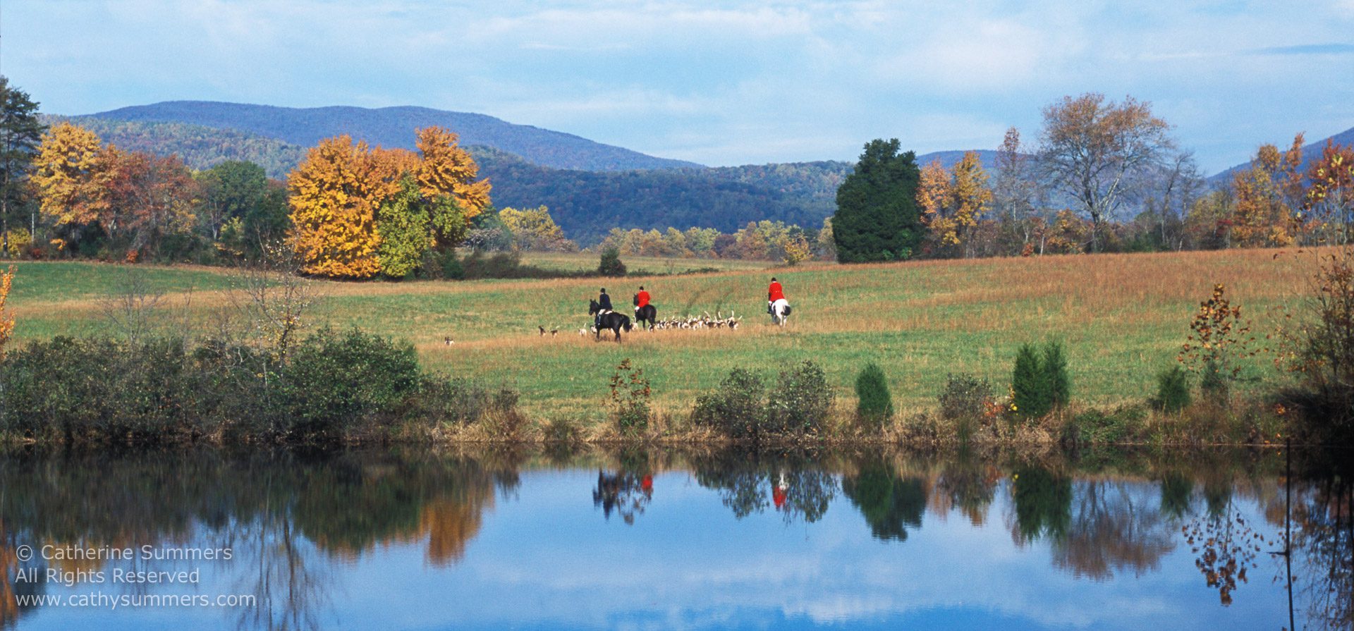 huntsman and staff across pond with reflection, fall trees and mountains in background
